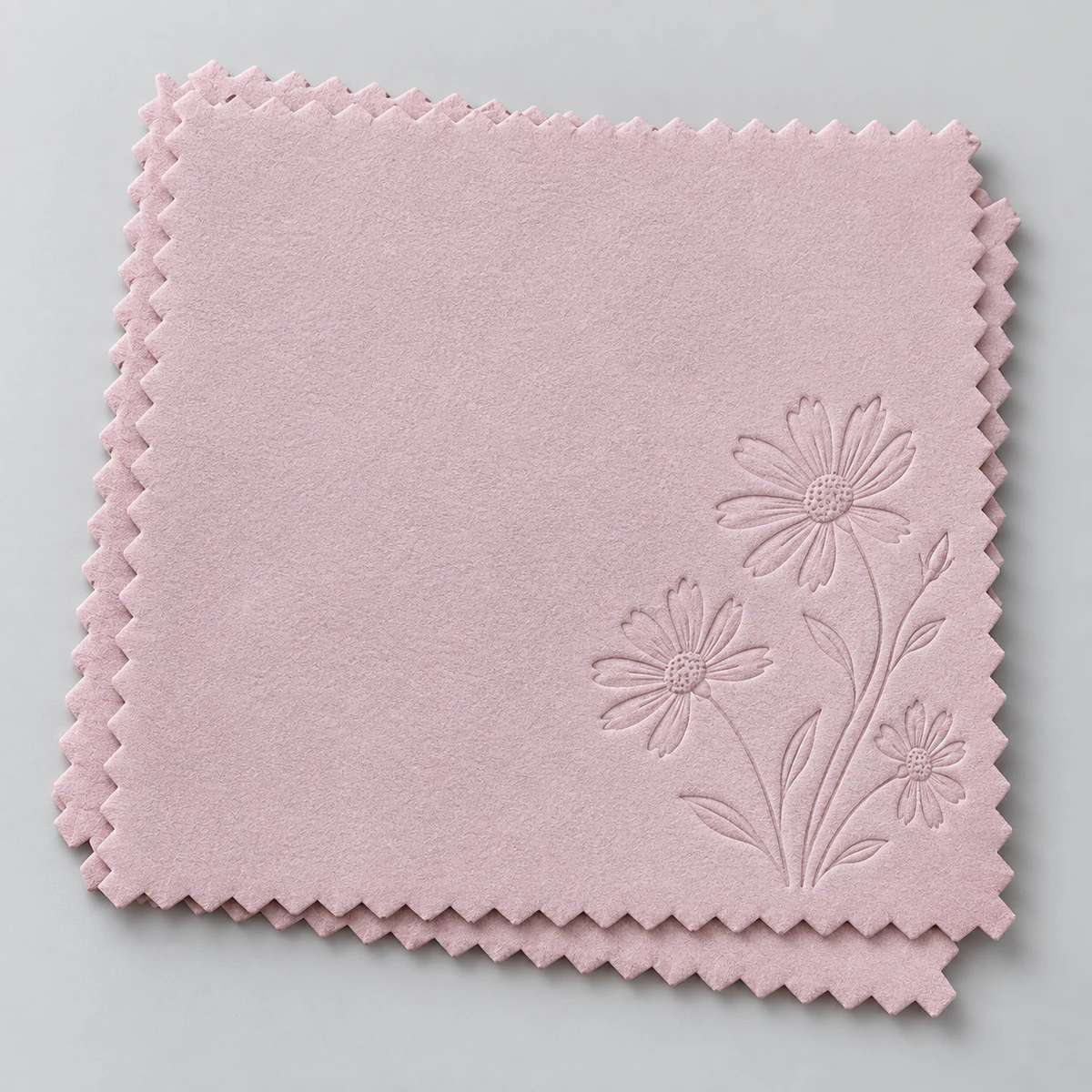 Stack of pink silver polishing cloths with an embossed daisy flower motif and zigzag edges