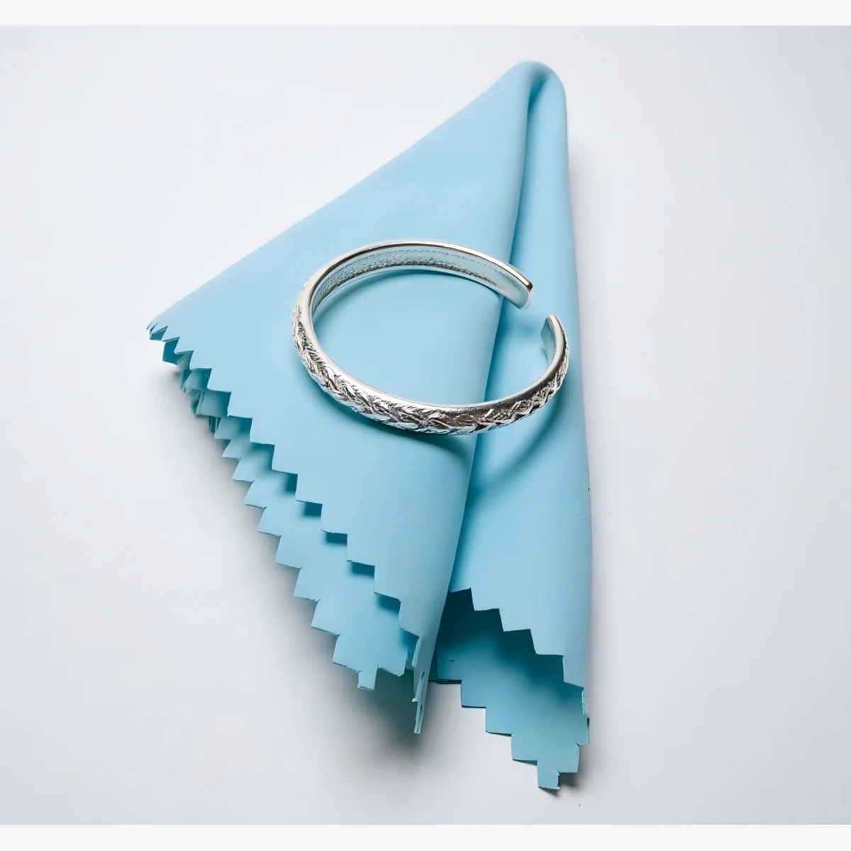 Blue 6.5 x 10 cm rectangular silver polishing cloth folded beneath a silver bracelet