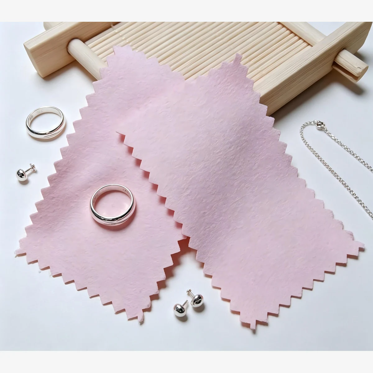Two pink 6.5 x 10 cm rectangular silver polishing cloths displayed with rings, earrings and a chain